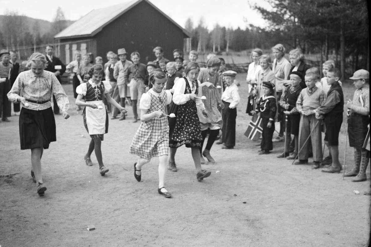 Schwarzes und weißes Foto von Kindern, die Fußball spielen, mit einer Menge, die Fahnen hält, im Hintergrund, Bäume und ein Haus.