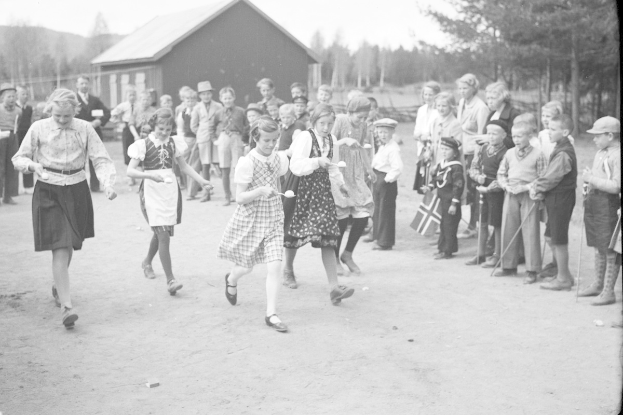 Schwarzes und weißes Foto von Kindern, die Fußball spielen, mit einer Menge, die Fahnen hält, im Hintergrund, Bäume und ein Haus.