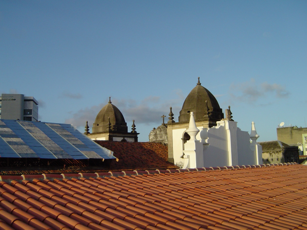 Stadtlandschaft mit mehreren Gebäuden im Vordergrund, einem klaren blauen Himmel im Hintergrund und Solarpanelen auf dem Dach eines Gebäudes.