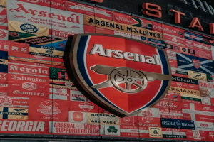 Das Arsenal FC-Logo ist auf einem Gebäude zu sehen, umgeben von Bannern, Fahnen und Schildern mit textbezogenen Inhalten zum Fußballclub.