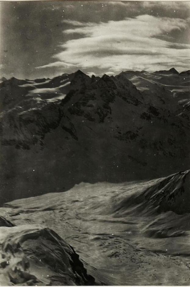Ein Schwarz-Weiß-Foto einer schneebedeckten Gebirgskette mit einem bewölkten Himmel und einem Text am unteren Rand, der 'Gustav Klimt - Die Alpen' lautet.