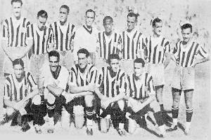 Ein Schwarz-Weiß-Foto einer Fußballmannschaft, bei der einige Spieler stehen und andere auf dem Boden sitzen, mit Text unten.