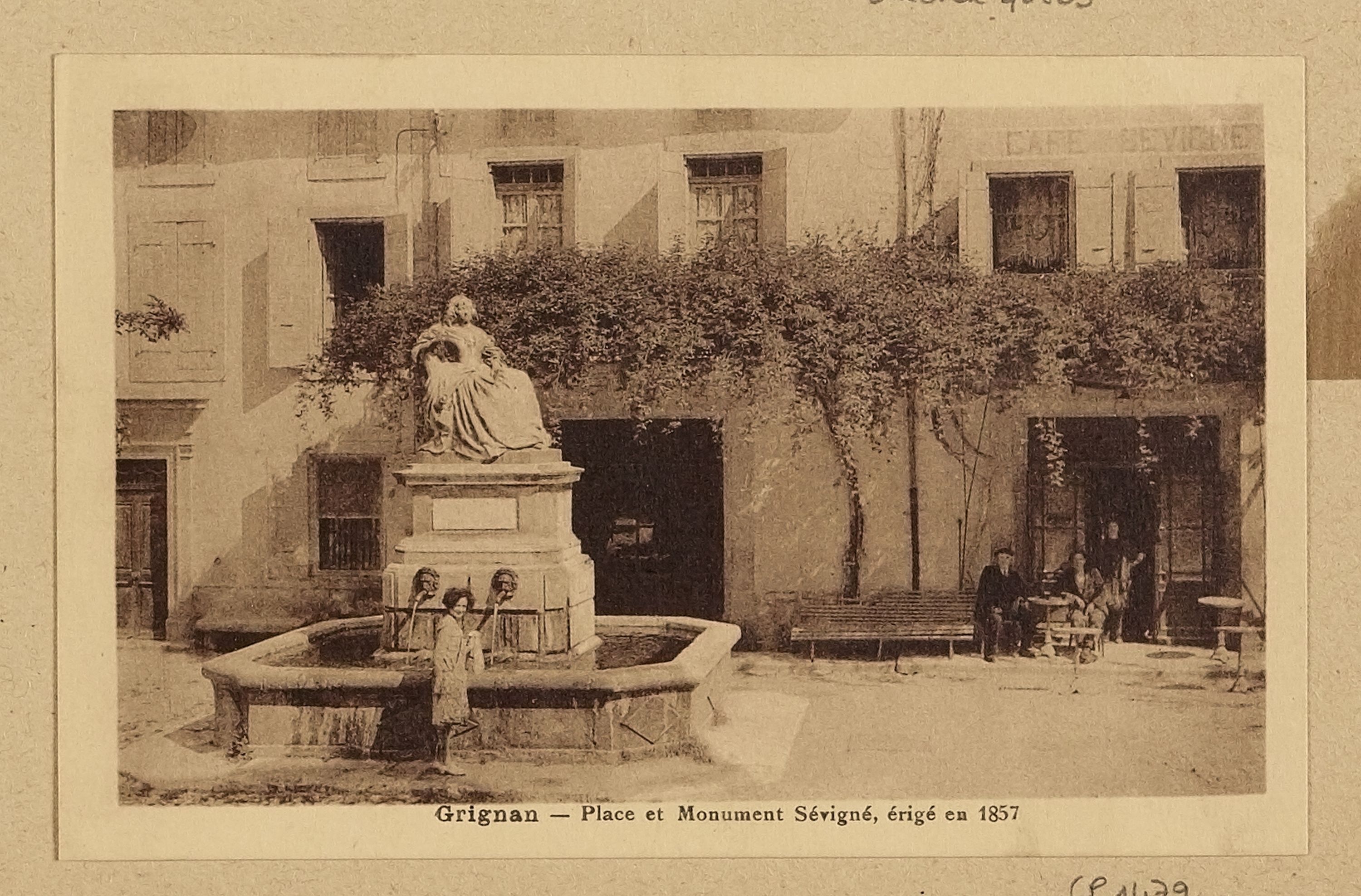 Ein altes Foto eines Brunnens mit einer Statue auf einem Sockel in der Mitte, umgeben von Menschen auf Bänken, mit einem Baum im Hintergrund und Text unten.