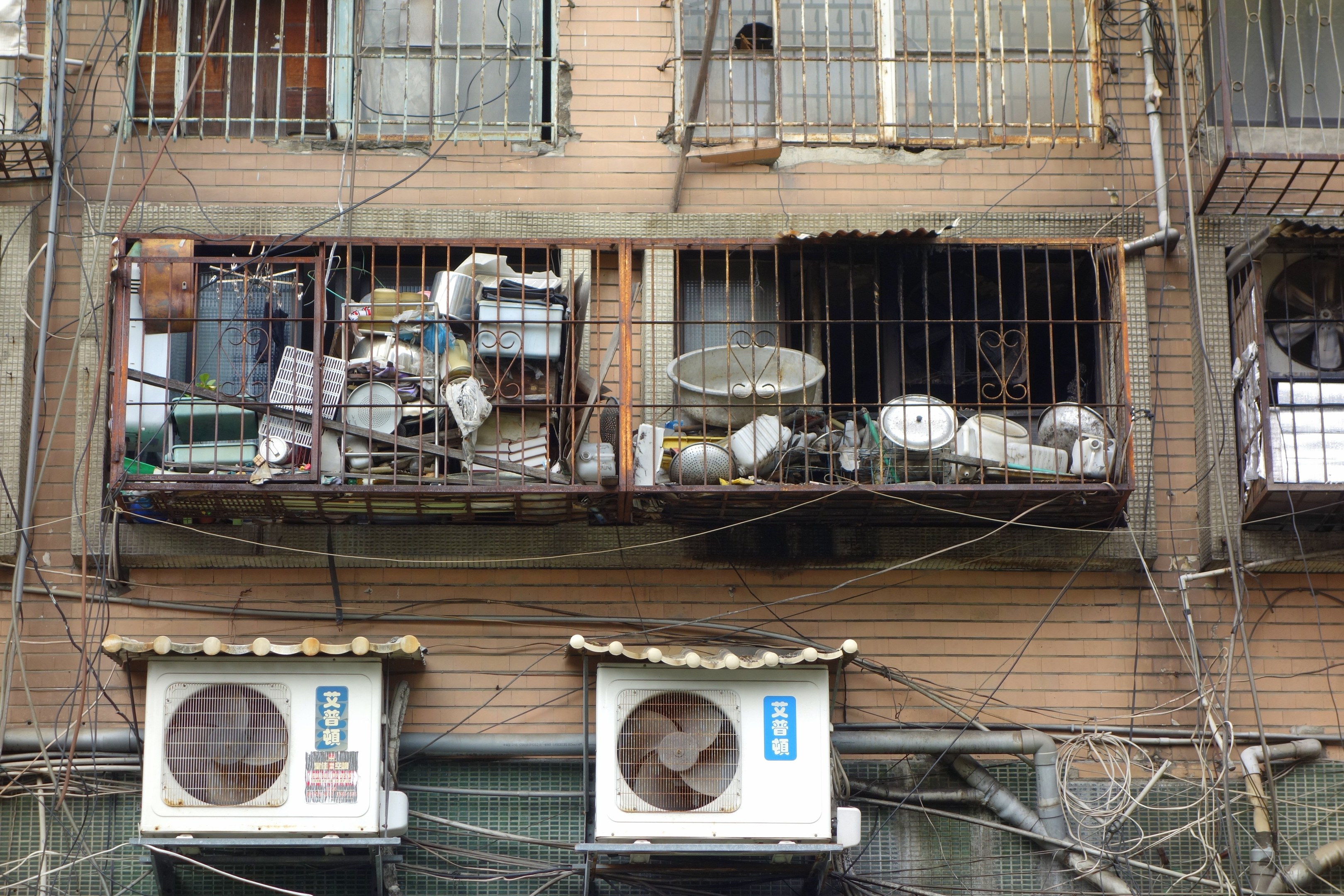 Wohngebäude mit Fenstern, Eisengittern, Klimaanlagen, Rohren und Drähten an der Außenseite.