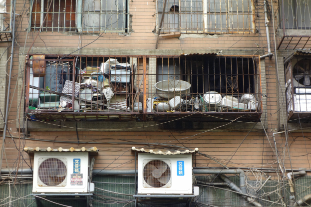 Wohngebäude mit Fenstern, Eisengittern, Klimaanlagen, Rohren und Drähten an der Außenseite.