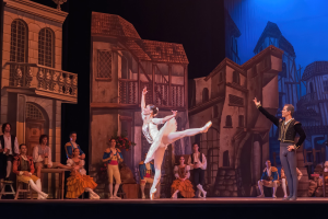 Zwei Tänzer performen auf einer Bühne im Royal Opera House in London, mit einem Publikum, das im Hintergrund sitzt und steht.