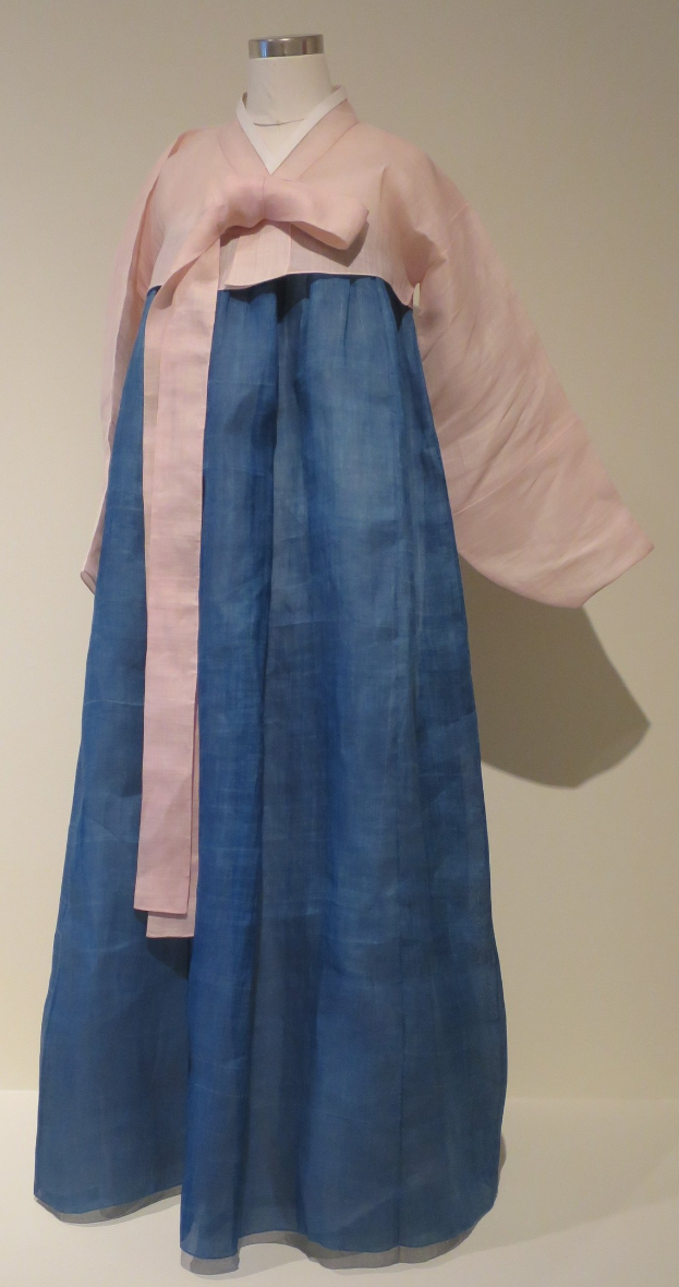 Eine Schaufensterpuppe in einem blauen und pinkfarbenen hanbok, einem traditionellen koreanischen Kleid, das in einem Museum mit neutralem Hintergrund ausgestellt ist.