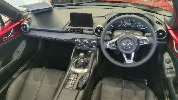 Rotes Mazda MX-5 Miata RF Interieur mit schwarzen Ledersitzen, Lenkrad, Schaltknüppel, Knöpfen, Bildschirm und Spiegel.