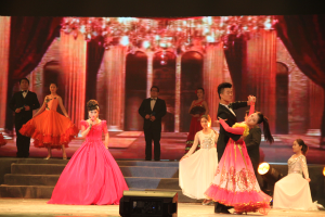 Eine Gruppe von Menschen auf einer Bühne mit Lichtern, Stufen und einem Hintergrundbild, mit einem Lautsprecher unten, der eine Tanzvorstellung suggeriert.