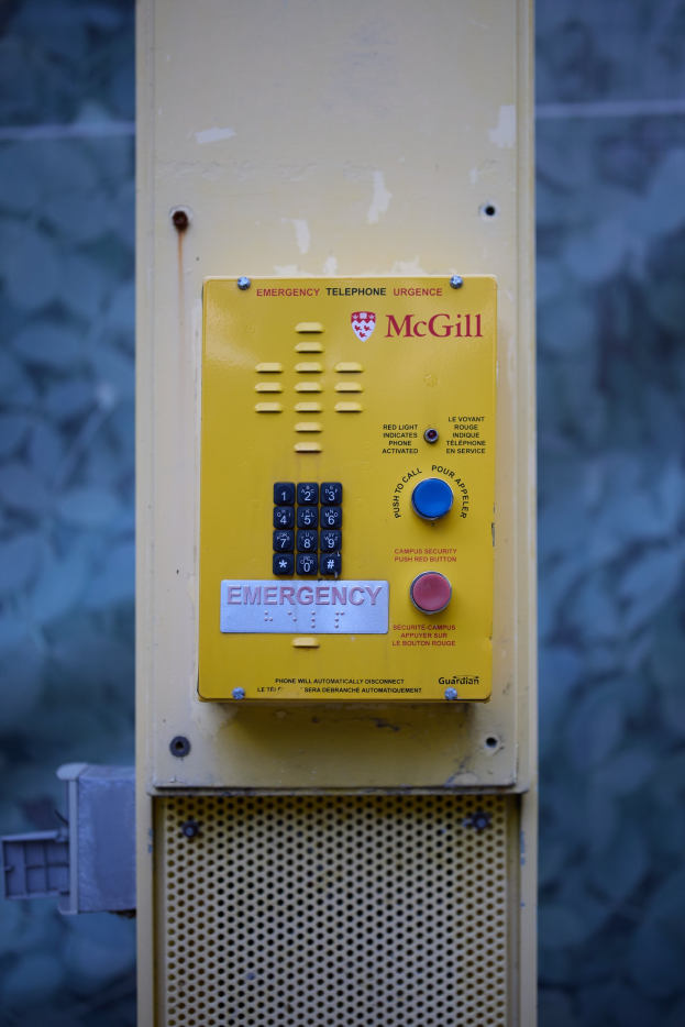 Gelber Notrufknopf an einer Gebäudewand montiert, mit Tasten und Text, der darauf hinweist, dass es sich um einen Notruf handelt.