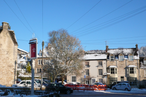 Fahrzeuge auf einer schneebedeckten Straße mit Häusern, Bäumen und Strommasten im Hintergrund.