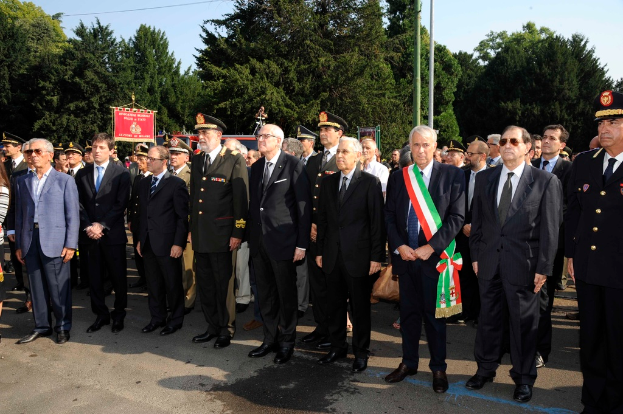 Eine Gruppe von Menschen in Anzügen, die draußen mit zwei Pfählen und Bäumen im Hintergrund stehen.
