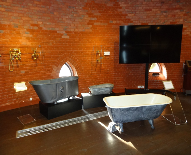 Ein gemütliches Badezimmer mit einer Backsteinwand, einer zentralen Badewanne, Wandhähnen auf der linken Seite und einem montierten Fernseher auf der rechten Seite.