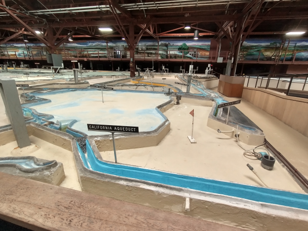 Ein großes Indoor-Wasserpark mit zahlreichen Wasserbahnen, Stangen, Texttafeln, Deckenleuchten und Wandgemälden, das wie ein Minigolfplatz gestaltet ist.