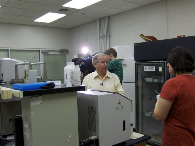 Ein Mann steht in der Mitte des Bildes, mit einer Frau rechts, einem Jungen hinter dem Mann, der Video aufnimmt, und Maschinen auf beiden Seiten.