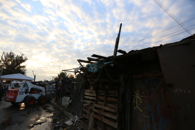 Ein Lastwagen parkt vor einem zerstörten Gebäude, umgeben von Menschen, Fahrzeugen, Zelten und Trümmern, unter einem bewölkten Himmel, was die Auswirkungen von Hurrikan Katrina illustriert.
