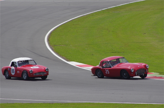 Zwei rote Autos auf einer Rollbahnrennstrecke mit einer Grasfläche auf der rechten Seite.
