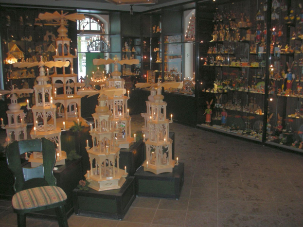 Ein Raum voller verschiedener Weihnachtsdekorationen, darunter ein Stuhl auf dem Boden, Spielzeuge auf Regalen und Deckenlichter mit einem Kronleuchter, der eine festliche Weihnachtsstimmung schafft.