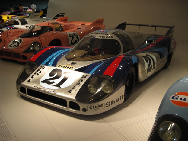 Ein Porsche 917K Rennwagen aus Le Mans in einem Museum neben anderen Sportwagen ausgestellt, mit Besuchern und Informationsschildern.