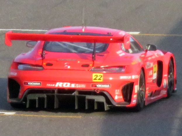 Roter Porsche 911 GTS Rennwagen auf einer Rennstrecke mit aerodynamischem Design, großem Heckspoiler und schwarzen Rädern.
