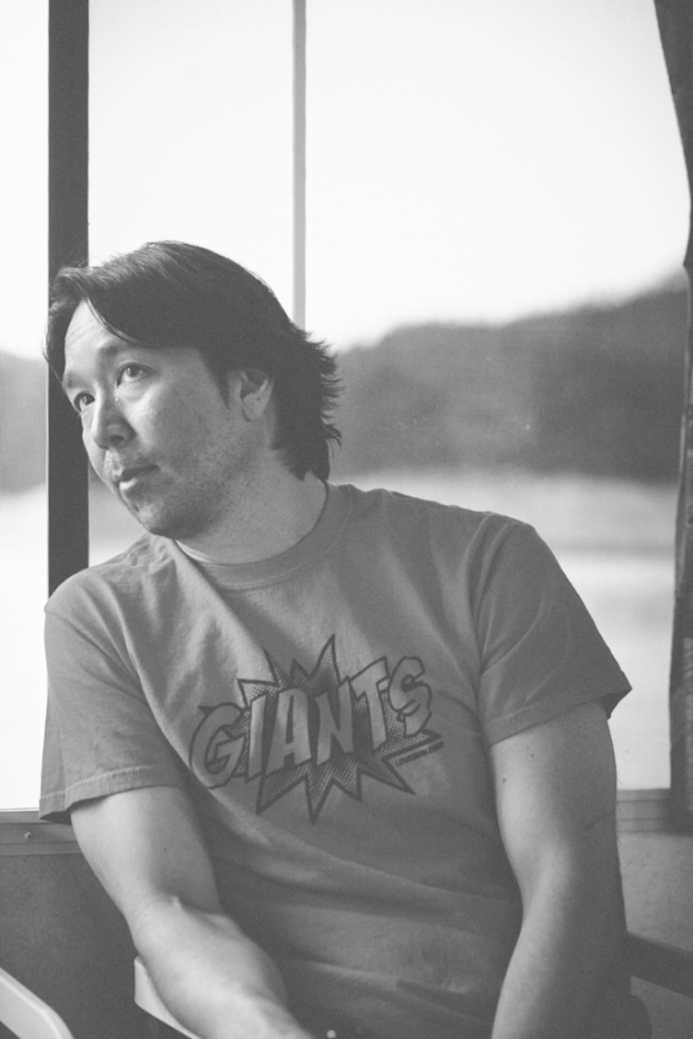 Ein Schwarz-Weiß-Bild eines Mannes in einem T-Shirt mit einem unscharfen Wort im Hintergrund.