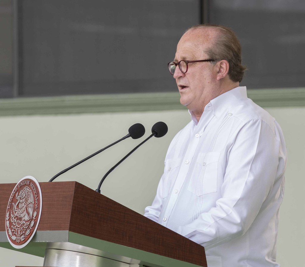 Ein Mann in einem weißen Hemd und Brille steht neben einem Rednerpult und spricht.
