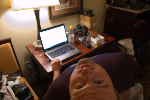 Eine Person, die in einem Stuhl sitzt und auf einem Laptop arbeitet, mit einer Lampe davor, die ihren Kopf nach oben neigt.