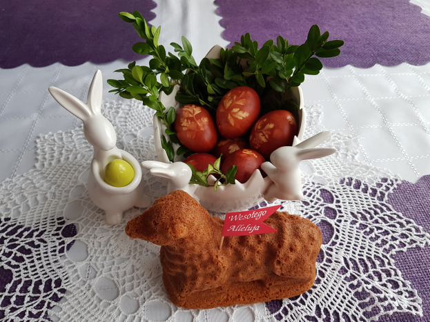 Ein Tisch mit einer Decke darauf h├Ąlt eine Schale voller bunter Ostereier mit Osterhasenfiguren darauf.