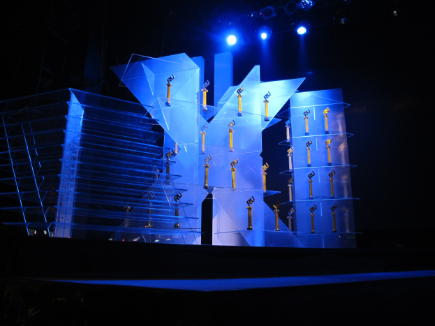 Eine Bühne für eine Preisverleihung mit dunklem Hintergrund, beleuchtet von ein paar Lichtern und mit mehreren Gegenständen, die mit dem Event in Verbindung stehen.