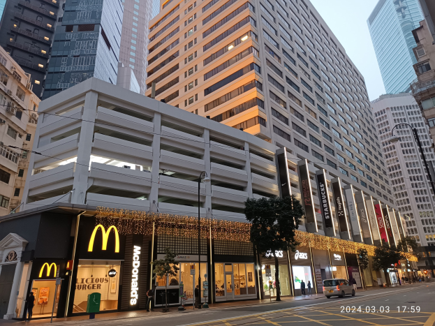 McDonald's-Restaurant auf einer belebten Stadtstraße mit hohen Gebäuden, Fahrzeugen, Fußgängern, Straßenmöbeln, Bäumen und einem klaren Himmel.