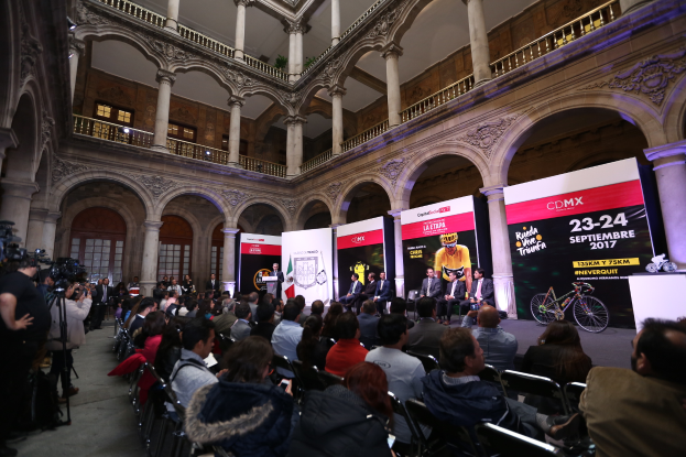 Eine Gruppe von Menschen, die an einem Tisch mit einem Podium und einem Mikrofon vor einer Menge, Kameras und Bannern sitzen, was auf eine Pressekonferenz für das CDMX 2017-Event hindeutet.