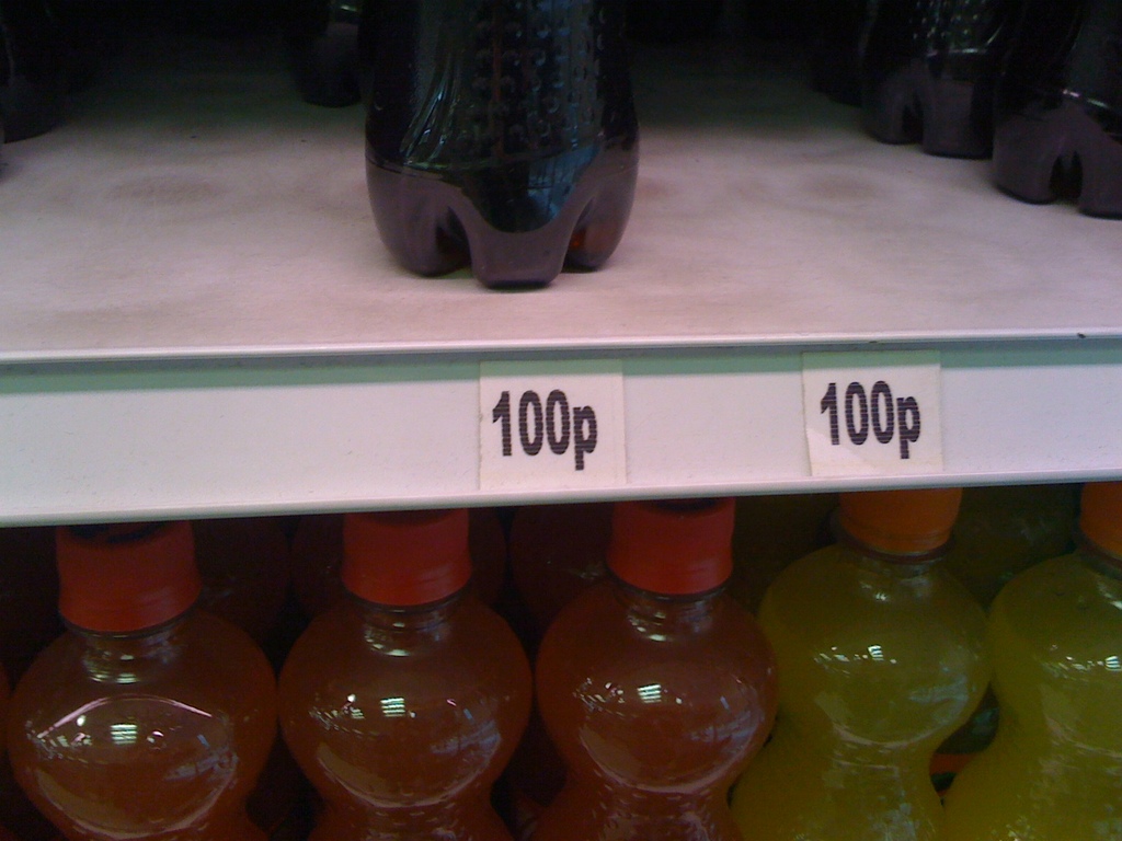 Flaschen in orange, gelb und schwarz sind in Regalen mit Preisschildern angeordnet.