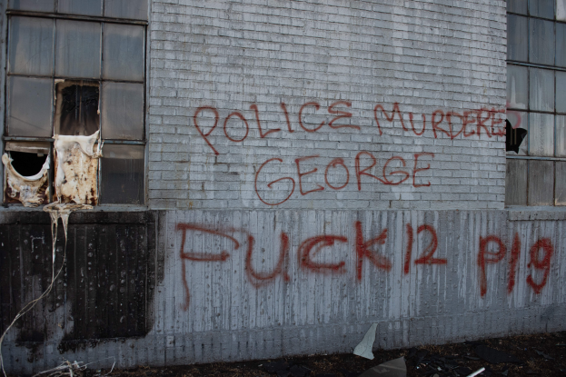 Ein Gebäude mit Graffiti, das "Polizei Mord George Fuck 12 P19" auf der Seite trägt, mit Fenstern und diversen Gegenständen vorne auf dem Boden.