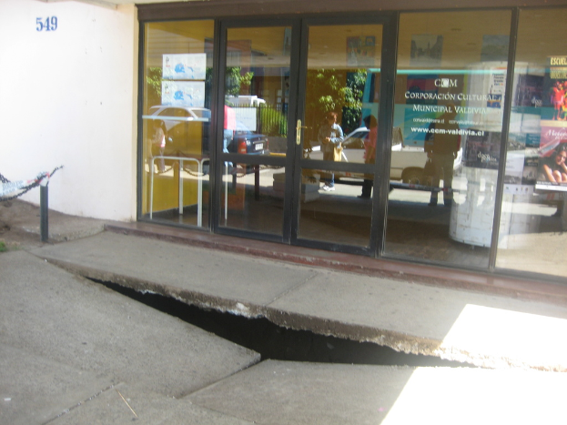 Eine gebrochene Oberfläche mit einer Glastür, Wand und Stange im Hintergrund, die sich bewegende Fahrzeuge und einige stehende Personen reflektiert.