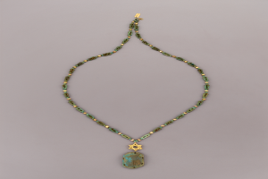 Eine goldene Kette mit einem grünen Davidstern-Anhänger mit einem Türkisstein, die auf einer flachen Oberfläche liegt.