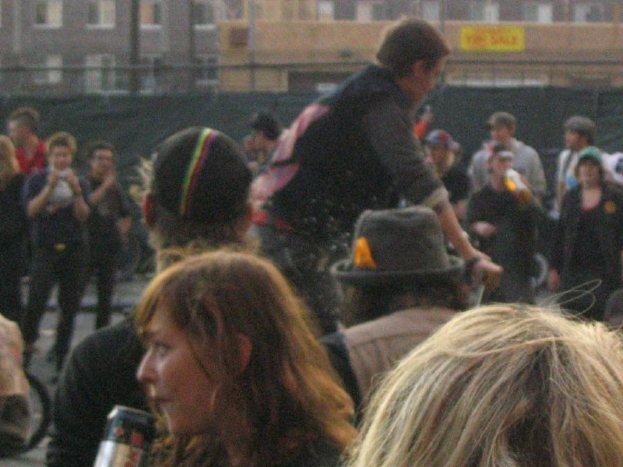 Eine Menge steht vor einem Zaun mit einer schwarzen Gardine und einem GebÃ¤ude im Hintergrund.